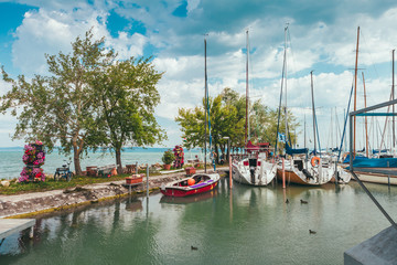 Fototapeta na wymiar View to entrance to Siofok harbor at Balaton lake, Hungary, with crystal clear water of emerald color, green coastline, puffy clouds on sky