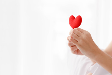 Close up woman's hand holding red heart with copy space on left side.