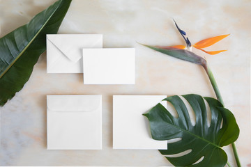 Empty card with envelope on marble table and tropical flowers. Mockup template with top view....