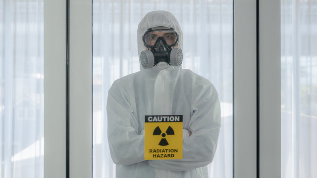 scientist with coverall protection clothing and full face protection mask in control room with radiation hazard sign