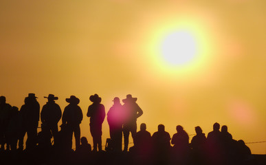 silhouettes of cowboys with hat and people on a sunset with intense sun the sky looks yellow and there are more than 10 people with them