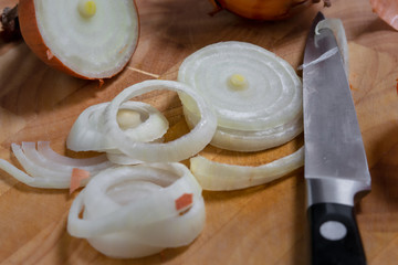Close up of sliced onion rings arranged on wooden cutting board, with a small kitchen knife