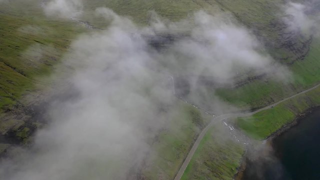 Fossá Waterfall on rugged Faroe Islands coastline, aerial reveal through clouds