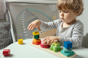 Beautiful toddler play with a wooden toys at home. Toddler play with a color educational toy.  Child play at the table in the baby room. Child development.  Funny baby. Lifestyle.