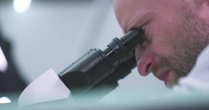Man working in laboratory looks into a microscope. Close-up.