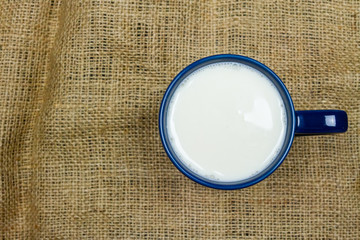 Top view of milk in blue ceramic cup or mug on sackcloth background with copy space. Milk is a high-protein beverage.