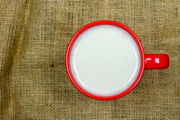 Top view of milk in red ceramic cup or mug on sackcloth background with copy space. Milk is a high-protein beverage, suitable for everyone. 