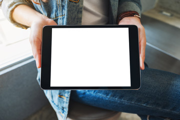 Mockup image of a woman holding and showing black tablet pc with blank white screen in cafe