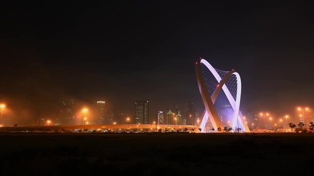 Wide timelapse of 5/6 Intersection Arches during night and fog rolling through the frame with West Bay skyscrapers in the background in Doha, Qatar.