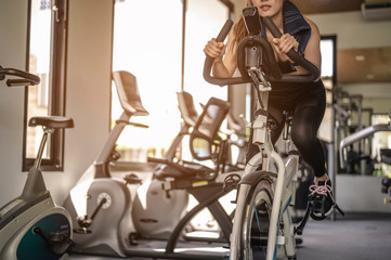 Front view of woman workout with bike. Women exercise working out in the gym for healthy lifestyle on bike at sunset. fitness ,workout, gym exercise ,lifestyle  and healthy concept.