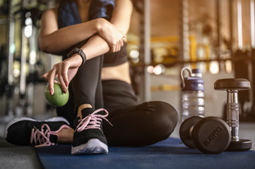 Woman sitting holding an apple after a workout in the gym at sunset. fitness ,workout, gym exercise ,lifestyle  and healthy concept.