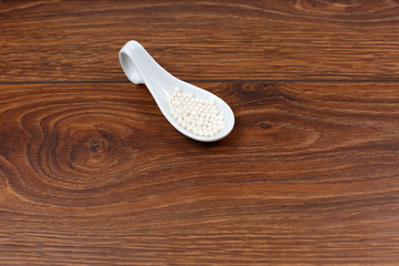 a spoon with homeopathic pills on wooden background.