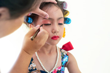 Closeup stylish little girl portrait with hair curlers having applied makeup by makeup artist