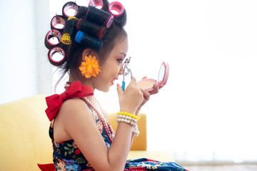 Fototapeta premium Stylish little girl portrait with hair curlers, little girl curling her eyelashes and looking in mirror, kid's fashion