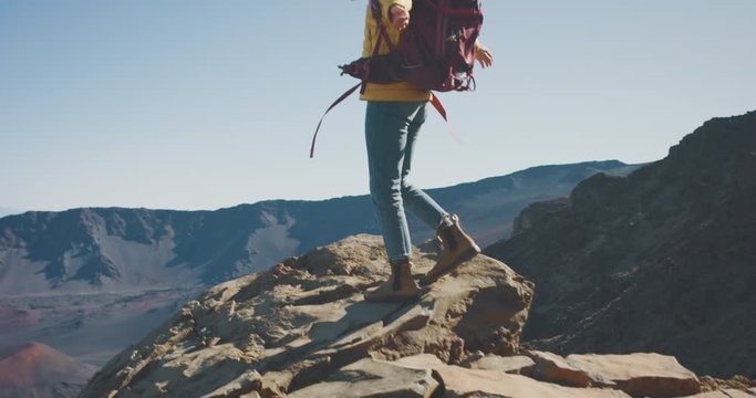 Young adventurous woman walking to the edge of a big cliff and raising her arms smiling, happy woman exploring the great outdoors on her weekend backpacking trip