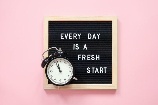 Every day is a fresh start. Motivational quote on black letter board and black alarm clock on pink background. Concept inspirational quote of the day. Greeting card, postcard