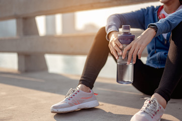 Young woman drink water and sitting to rest after jogging a morning workout in the city. A city...
