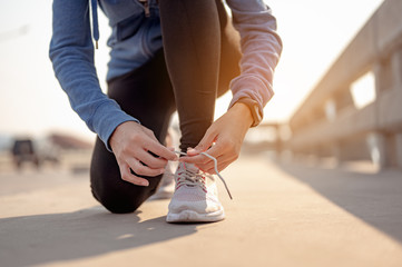 Young women using their hands to tie their shoes jogging in morning workout at the city. A city that lives healthy in the capital. Exercise, fitness, jogging, running, lifestyle, healthy concept.. - obrazy, fototapety, plakaty