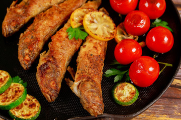 Delicious fried fish served with vegetables on black skillet. Close up.