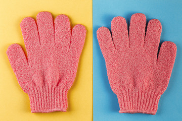 A pair of pink massage gloves for shower on blue and yellow background. Gloves for use in the shower for massage and scrub. Beauty background with cosmetic products. Beauty, health and spa concept