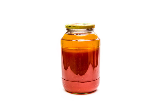 Glass jar with tomato juice on a white background close-up.