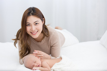 Obraz na płótnie Canvas Portrait of Beautiful mom lying at the back of the baby while the infant is sleeping on the white bed. Asian mother looking and touching the baby's hand which is her child with love and care.