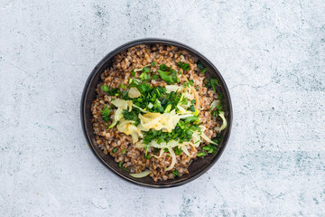 Russian, Ukrainian traditional cooked buckwheat grain porridge in bowl with parsley, herbs, onion, butter. Vegan vegetarian diet food. Homemade