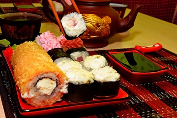 Japanese cuisine, rolls and sushi,lunch in Japanese,eat with chopsticks,tea ceremony,red sushi dishes, clay teapot and mugs