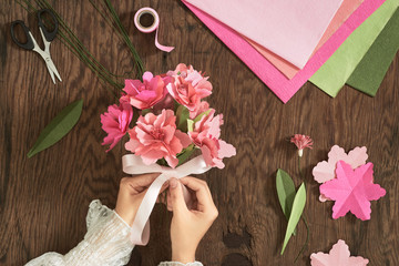 Woman making paper bouquet at wood table with color papers, scissors for valentines, holidays. Flatlay, top view.