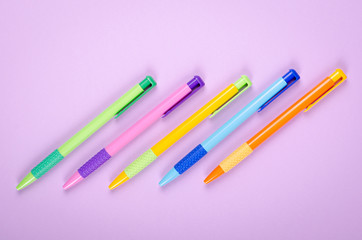 Different colored pens, school ballpoint on purple background composition.