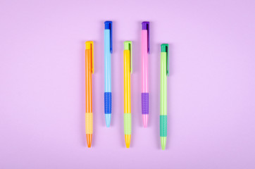 Different colored pens, school ballpoint on purple background composition.