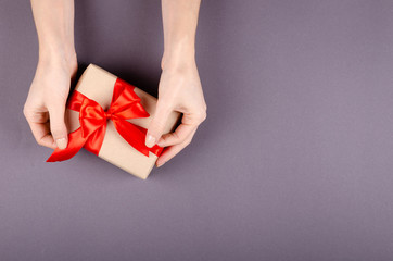 Hands with gift box on dark background composition, present with ribbon and bow.