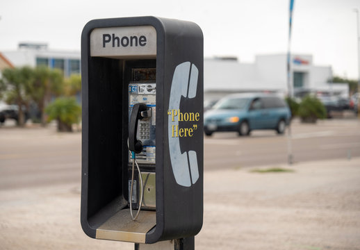 Public Pay Phone, coin operated, next to a busy street is an old and dirty analog type, but still in working condition as traffic drives by in background.