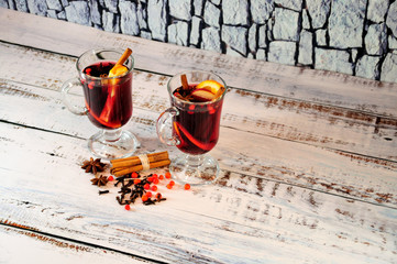 Two glass glasses of hot wine with orange, apple and cinnamon stand on a wooden table in a...
