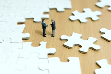 Business strategy conceptual photo - Miniature businessman make handshake partnership in the center of jigsaw puzzle piece 