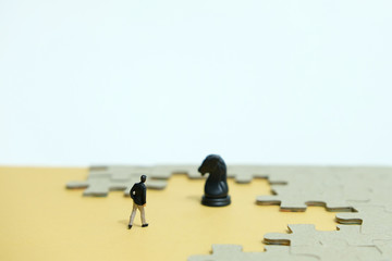Business strategy conceptual photo - Miniature businessman walking into horse knight pawn in the middle of jigsaw puzzle