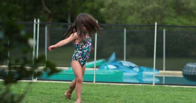 Little girl child playing by herself spinning around in swimwear in backyard garden