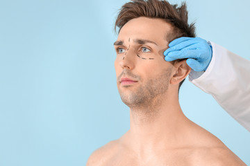 Obraz premium Plastic surgeon touching face of young man on color background