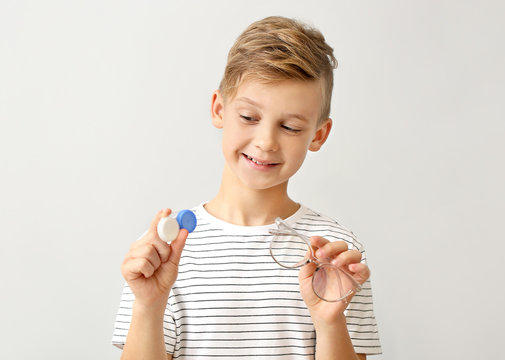 Little boy with contact lens case and eyeglasses on grey background