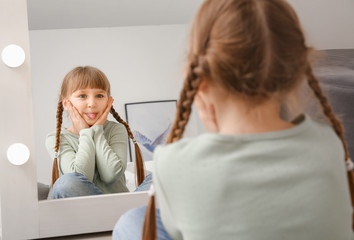 Funny little girl looking in mirror at home