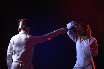 Toned photo of young fencers on dark background