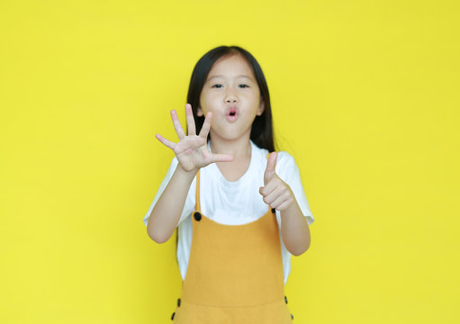 Little asian child girl showing finger number six isolated on yellow background. Kid counting with fingers for education concept. Selected focus at his hand