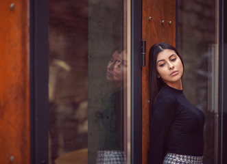Fototapeta premium Beautiful woman with long black hair standing near the large windows and looking at the camera