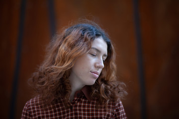 Fototapeta premium Dreaming young woman with spectacular curly red ginger hair looking at camera posing outdoor in downtown street. Female portrait.