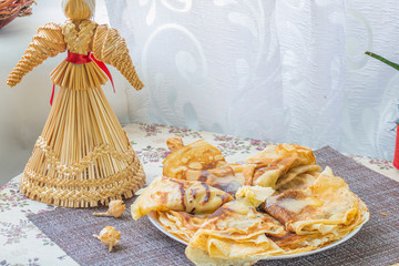 still life with pancakes and a straw doll of a traditional Slavic carnival Ukraine, Russia, Belarus - the celebration of the end of winter. pile of pancakes with butter on a table with a straw doll.