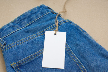 Mock-up of a white tag for clothes on blue jeans. Empty place for an inscription. Shop and sale.