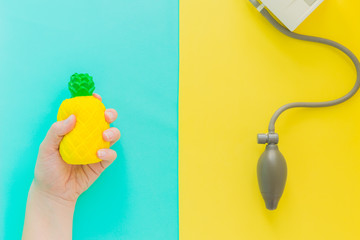Flat lay stress, antistress: toy squish yellow pineapple in hand, blood pressure monitor.Bright blue background.Compressing, soft,squeezable items to relieve,problems,anxieties,worries.Summer concept