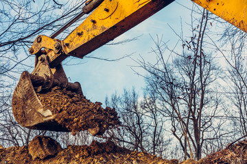 Backdrop of excavator bucket with soil on forest and sky background.