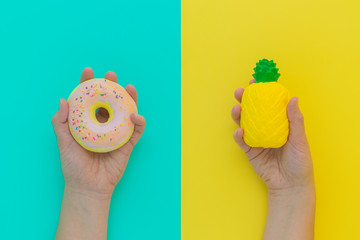 Flat lay antistress squish toys yellow pineapple,pink donut with sprinkles in hands.Bright blue background.Compressing,soft,squeezable items to relieve stress,problem,anxieties,worries.Summer concept