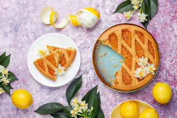 Delicious lemon pie slices with fresh lemons and a cup of tea on light background,top view